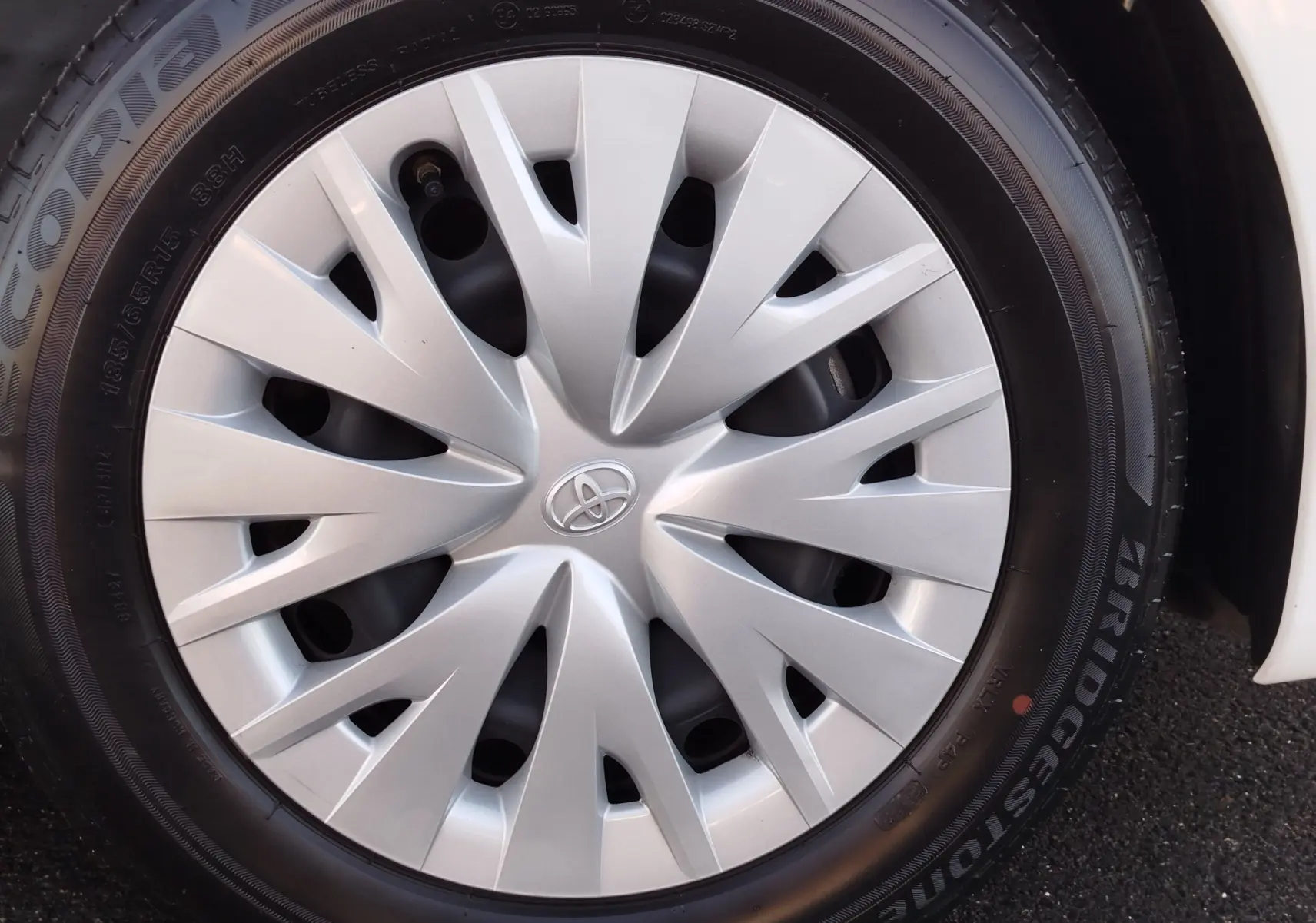 Gros plan sur la roue avant droite d'une Toyota Yaris blanche avec enjoliveur argenté au design étoilé.