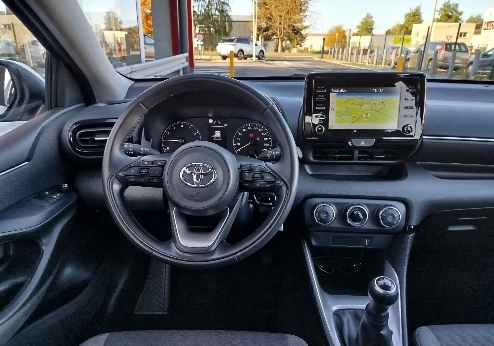 Vue intérieure avant de la Toyota Yaris blanche 2023, volant multifonction, écran tactile avec navigation et boîte manuelle.