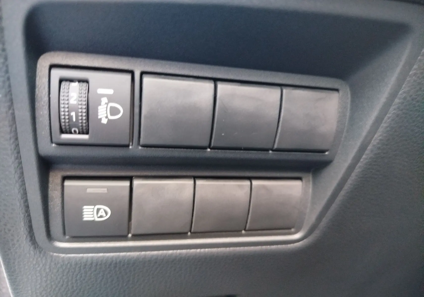 Gros plan sur les commandes noires de réglage des phares et de l’éclairage automatique dans une Toyota Yaris blanche.