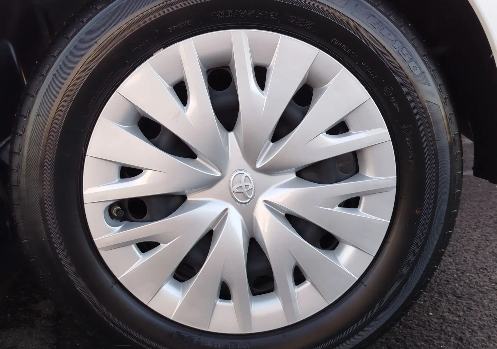 Gros plan sur la roue avant droite d'une Toyota Yaris blanche avec enjoliveur argenté au design moderne.