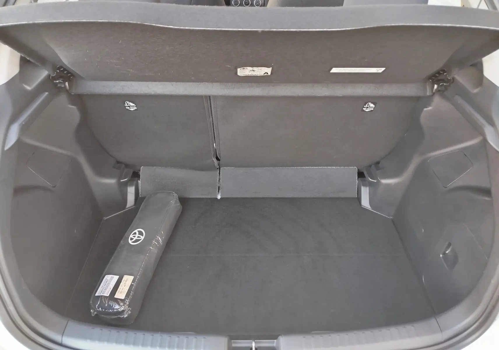 Coffre ouvert d'une Toyota Yaris blanche 2023, montrant un espace de rangement noir avec un kit Toyota posé à gauche.