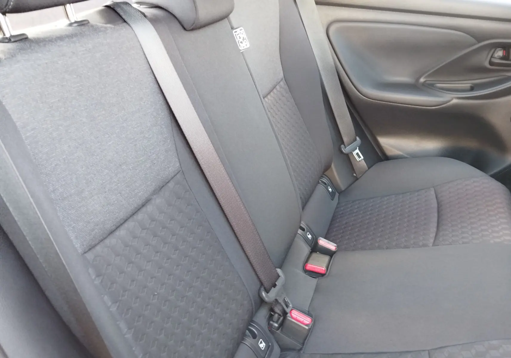 Vue intérieure du siège arrière droit de la Toyota Yaris 2023, tissu gris foncé avec ceinture de sécurité visible.