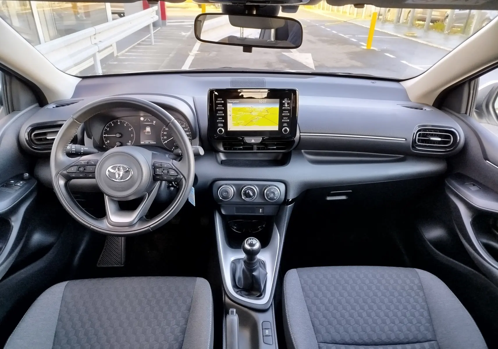 Vue intérieure avant de la Toyota Yaris blanche 2023, tableau de bord avec écran tactile et volant multifonction.