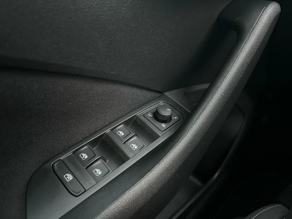 Gros plan sur les commandes de lève-vitres et rétroviseurs noirs à l'intérieur côté conducteur du Skoda Kamiq gris clair 2025.