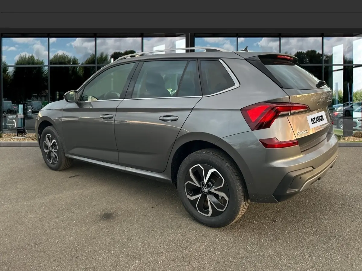 Vue 3/4 arrière droite d'un Skoda Kamiq gris clair avec jantes alliage et feux arrière LED, stationné devant une vitrine.