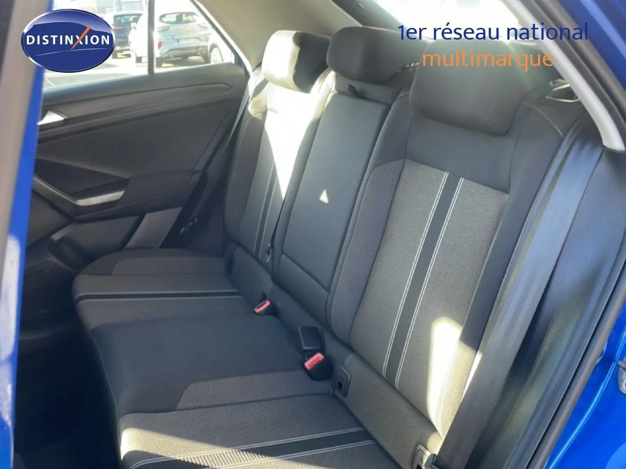 Vue intérieure côté arrière droit du Volkswagen T-Roc bleu Ravenna, montrant les sièges arrière en tissu gris avec surpiqûres blanches.