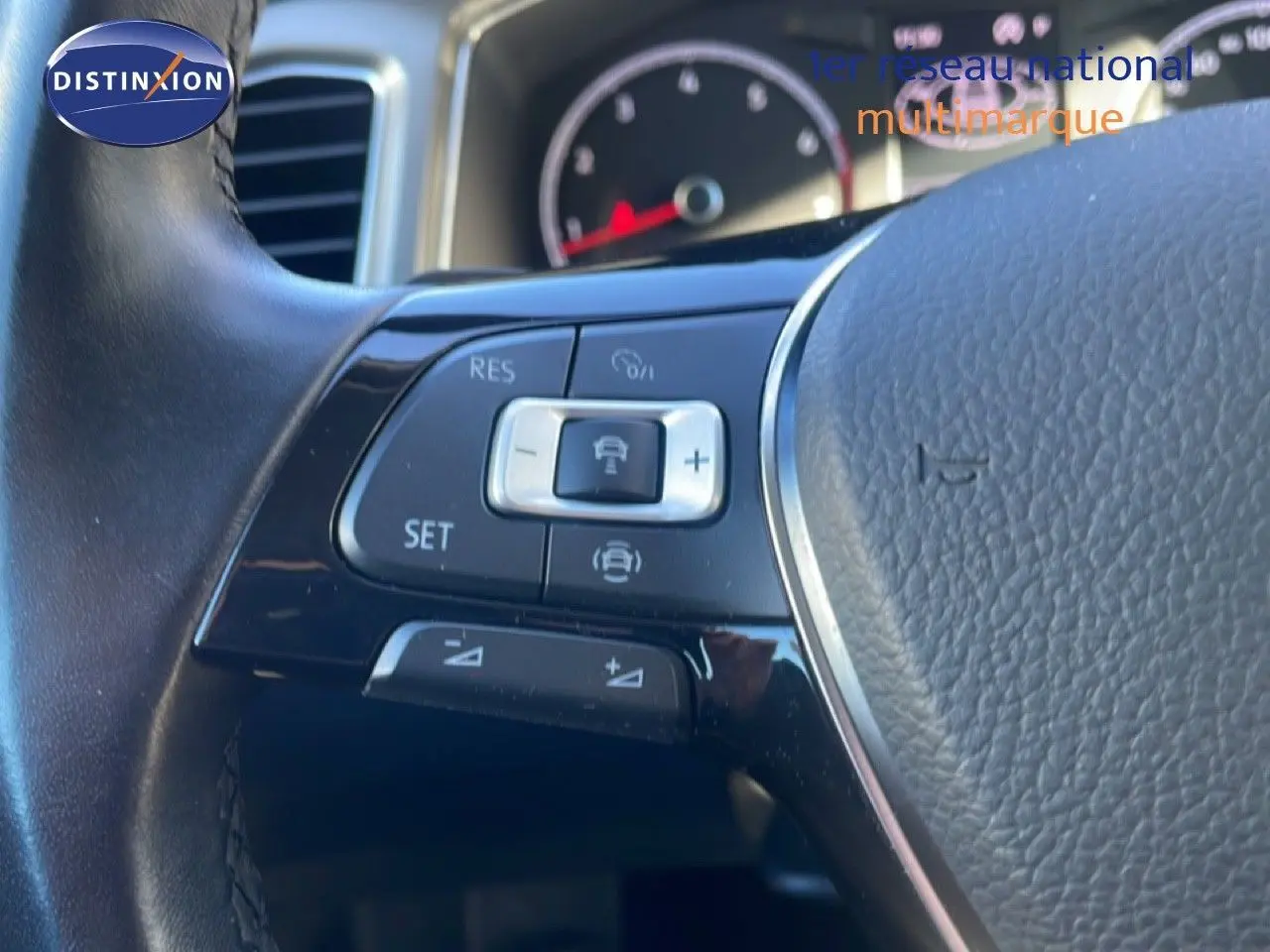 Gros plan sur les commandes de régulateur de vitesse au volant cuir noir du Volkswagen T-Roc 1.5 TSI bleu Ravenna.