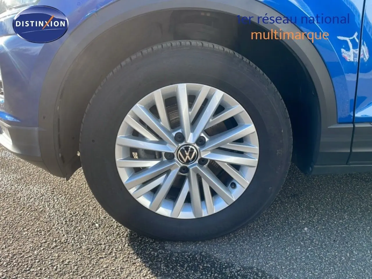 Gros plan sur la roue avant gauche d'un Volkswagen T-Roc bleu Ravenna métallisé, avec jante alliage argentée.