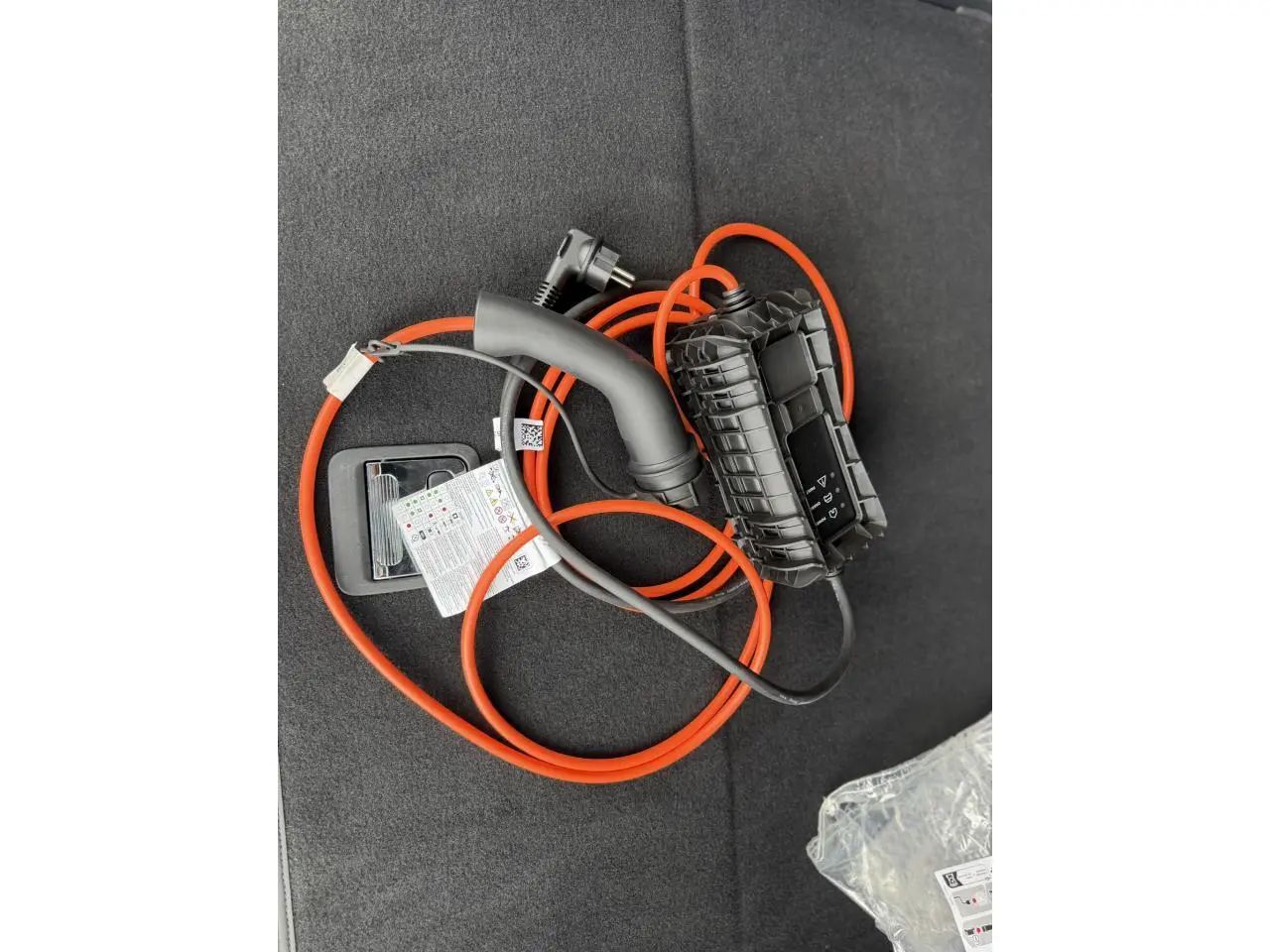 Câble de recharge orange posé dans le coffre d’un Peugeot 3008 Plug-in Hybrid noir Perla, vue intérieure.