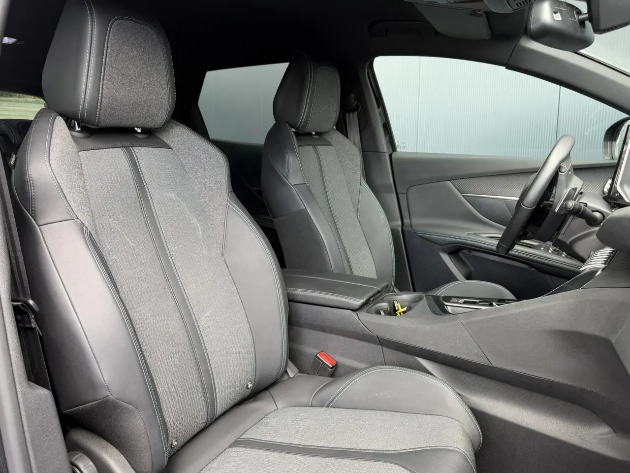 Vue intérieure côté droit du Peugeot 3008 2024, sièges bi-matière gris et noir avec accoudoir central fermé.
