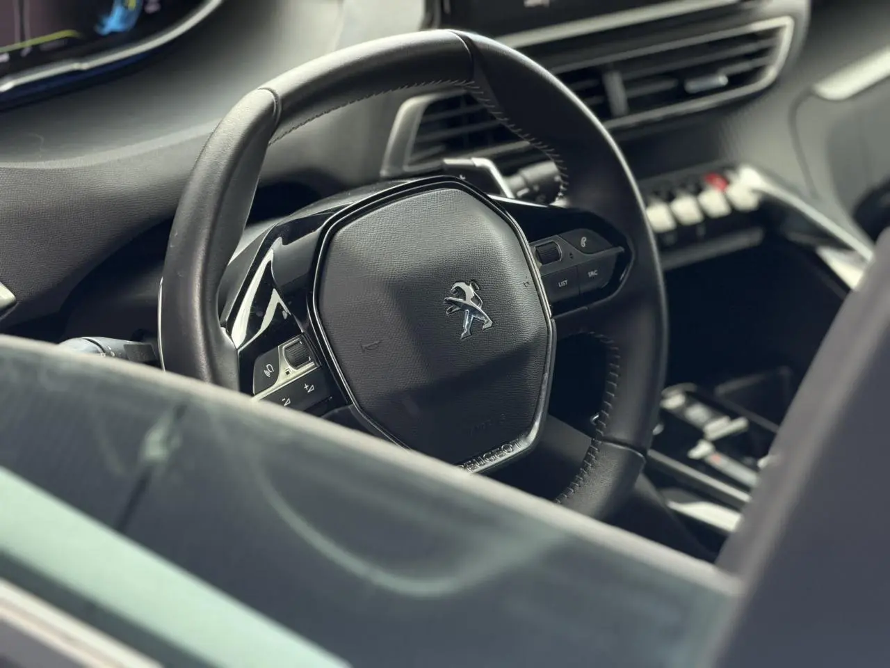 Vue rapprochée du volant noir cuir du Peugeot 3008 2024 avec commandes intégrées et tableau de bord sombre.