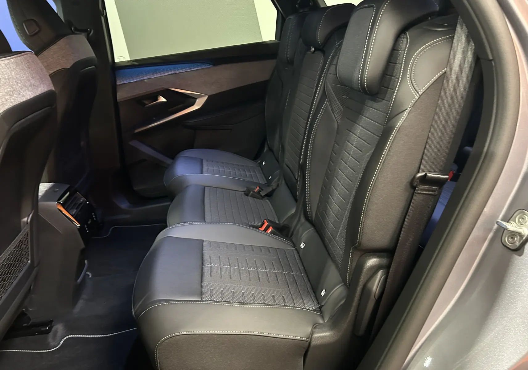Vue côté droit des sièges arrière en cuir et tissu gris du Peugeot 5008 III GT Hybrid 145 e-DCS6 avec porte ouverte.