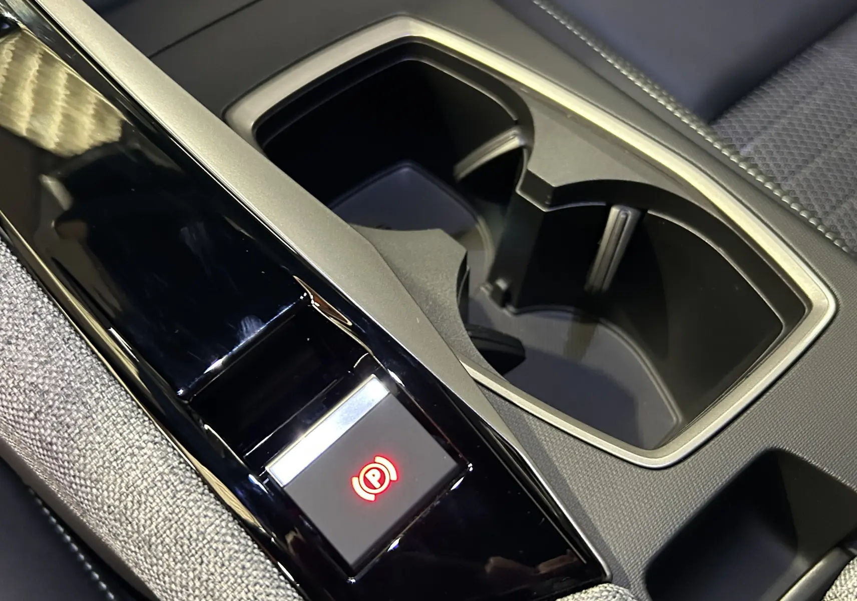 Gros plan sur la console centrale noire brillante avec bouton frein à main électronique et porte-gobelets du Peugeot 5008 gris Artense.