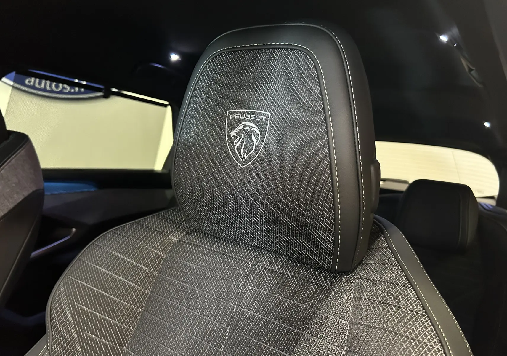 Gros plan sur l'appui-tête avant avec logo Peugeot brodé, intérieur sombre du SUV 5008 hybride 2025.
