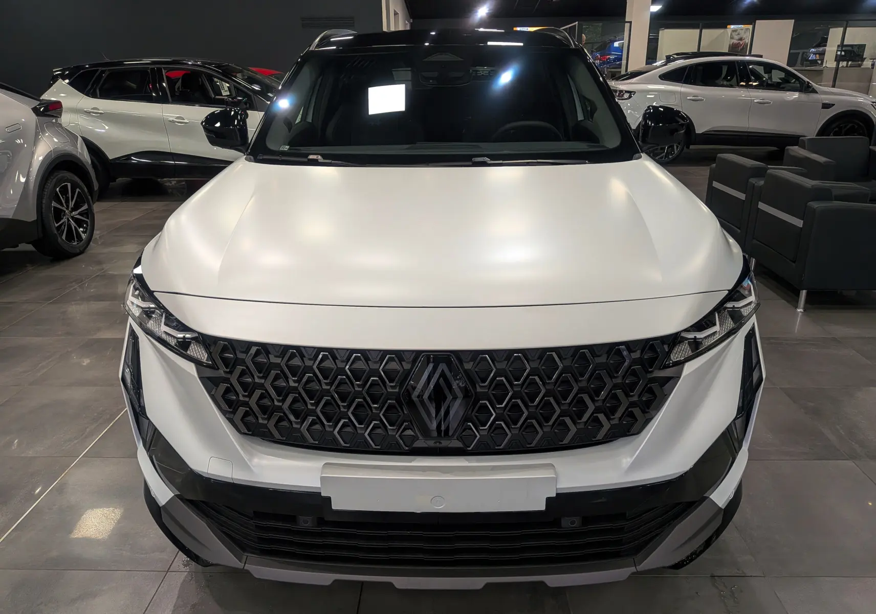 Vue frontale du Renault Austral blanc nacré satin avec toit noir, mettant en valeur sa calandre hexagonale et ses phares fins.