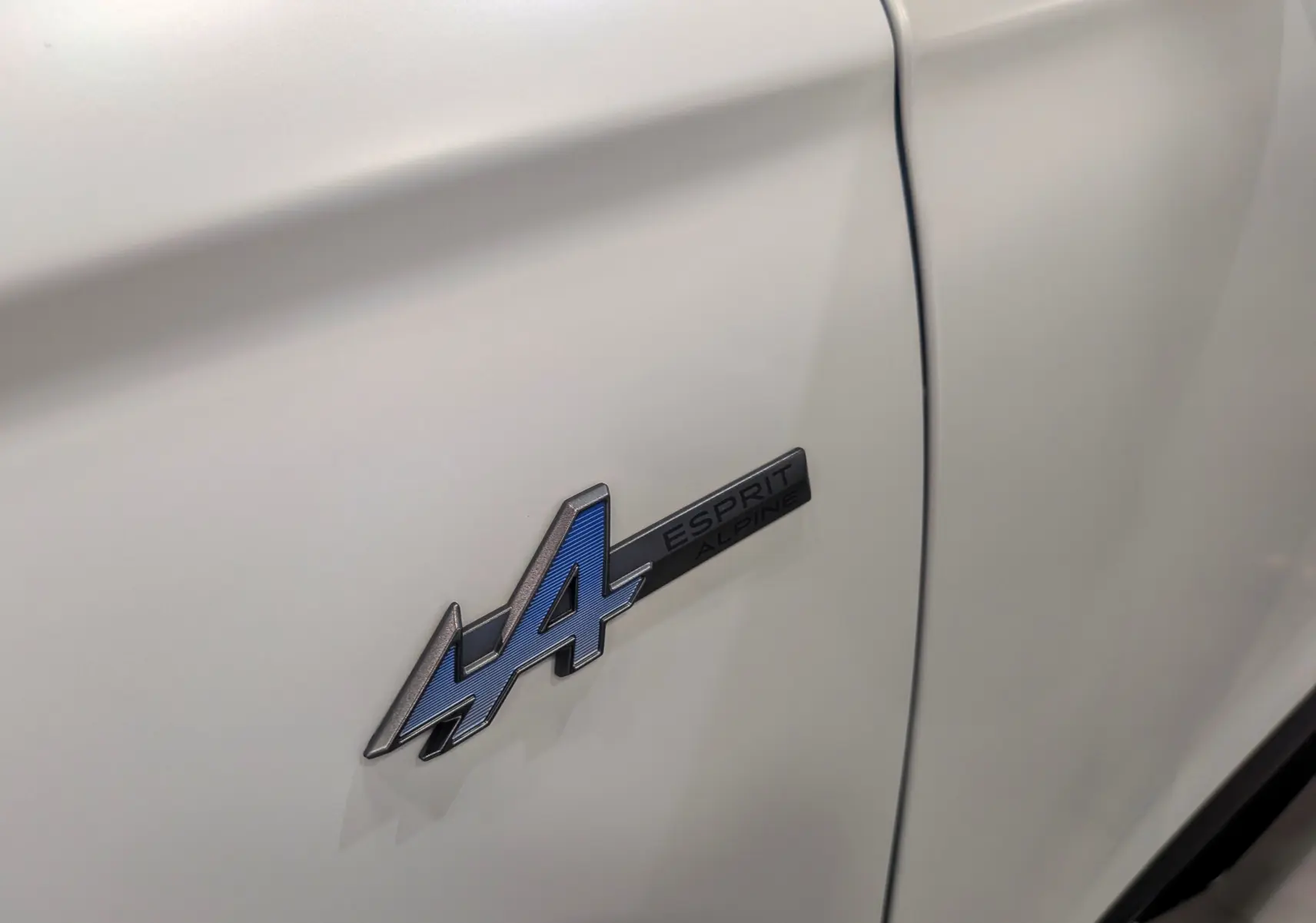 Gros plan sur l'emblème Esprit Alpine bleu sur la porte blanche nacrée satinée du Renault Austral 2025.