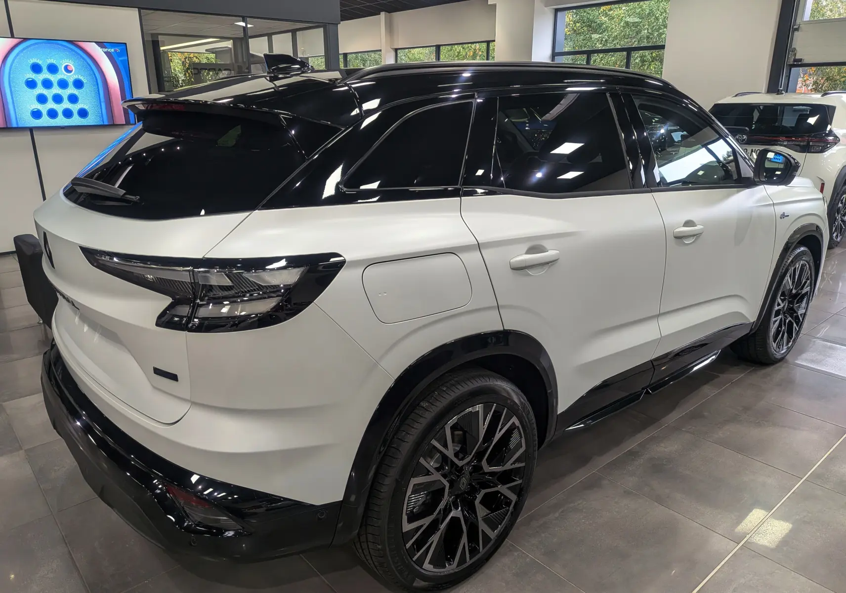 Vue 3/4 arrière droit du Renault Austral blanc nacré satin avec toit noir et jantes noires en concession.