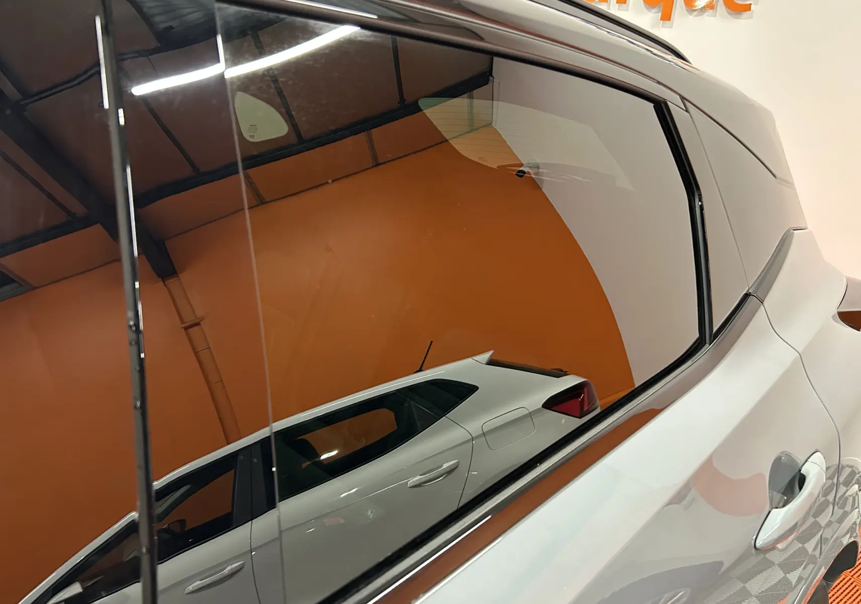 Reflet latéral droit du Nissan Qashqai gris céramique métal avec lignes de carrosserie marquées sur fond orange.