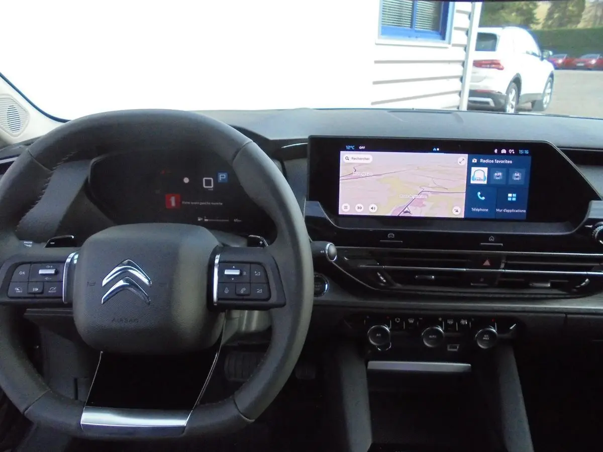 Vue intérieure du poste de conduite du Citroën C5 X gris platinum, avec volant multifonction et écran tactile central allumé.