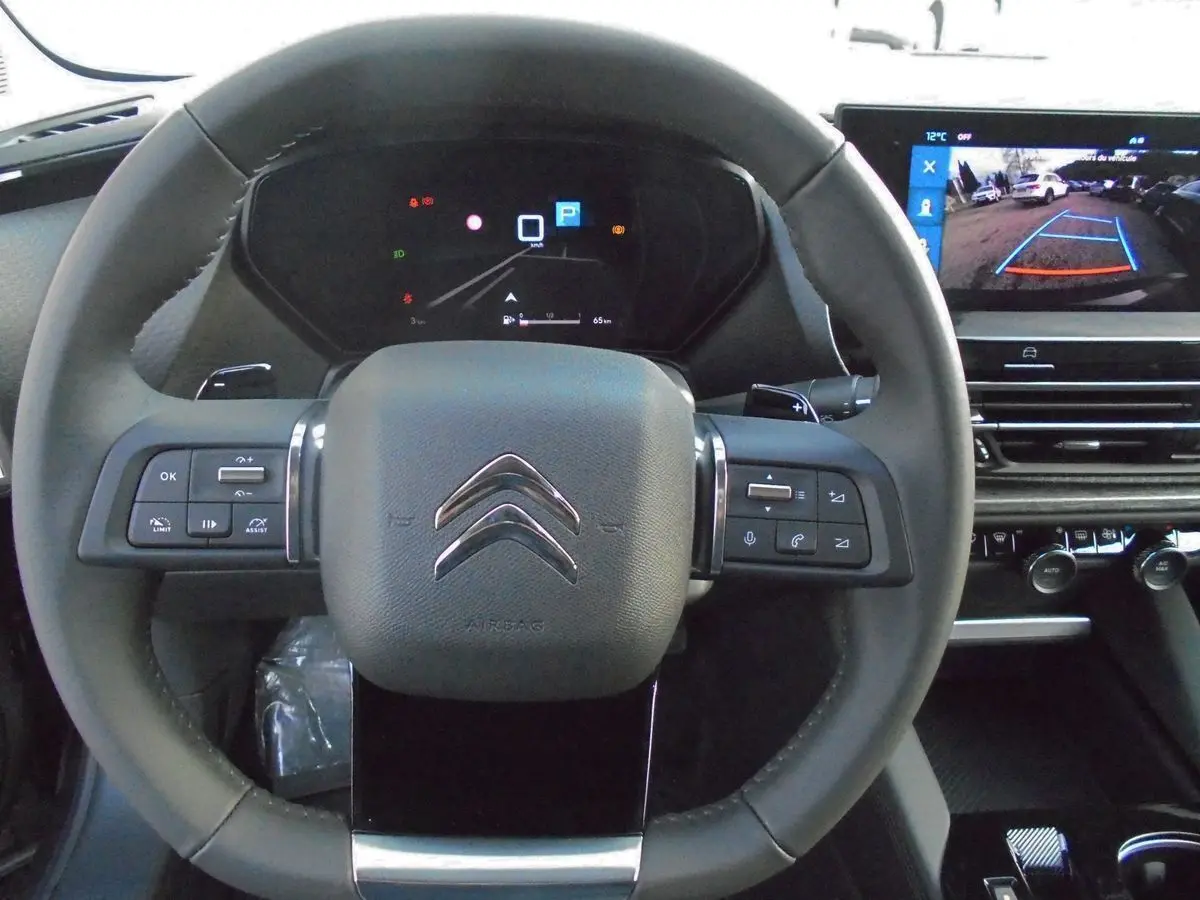 Vue intérieure centrée sur le volant noir de la Citroën C5 X 2022 avec tableau de bord digital et écran multimédia affichant la caméra de recul.