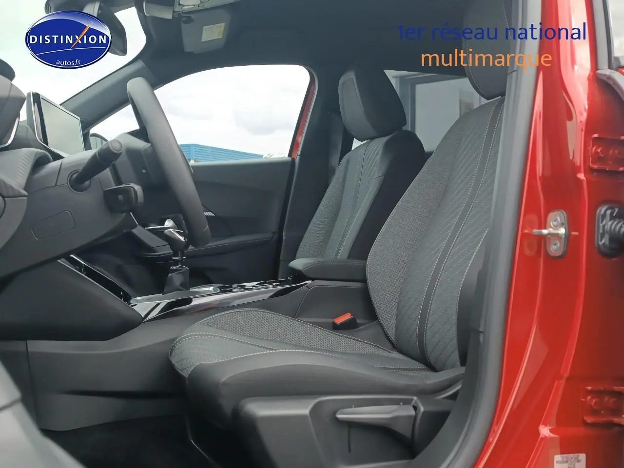 Vue intérieure côté conducteur de la Peugeot 2008 rouge elixir, mettant en valeur les sièges en tissu gris et la console centrale.