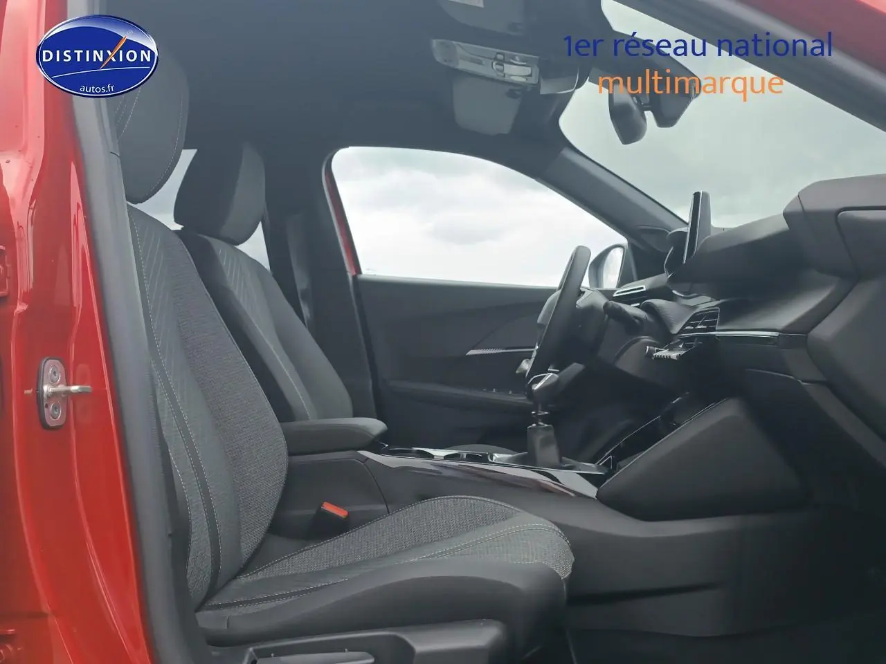 Vue intérieure côté conducteur de la Peugeot 2008 rouge elixir, montrant sièges tissu et tableau de bord moderne.