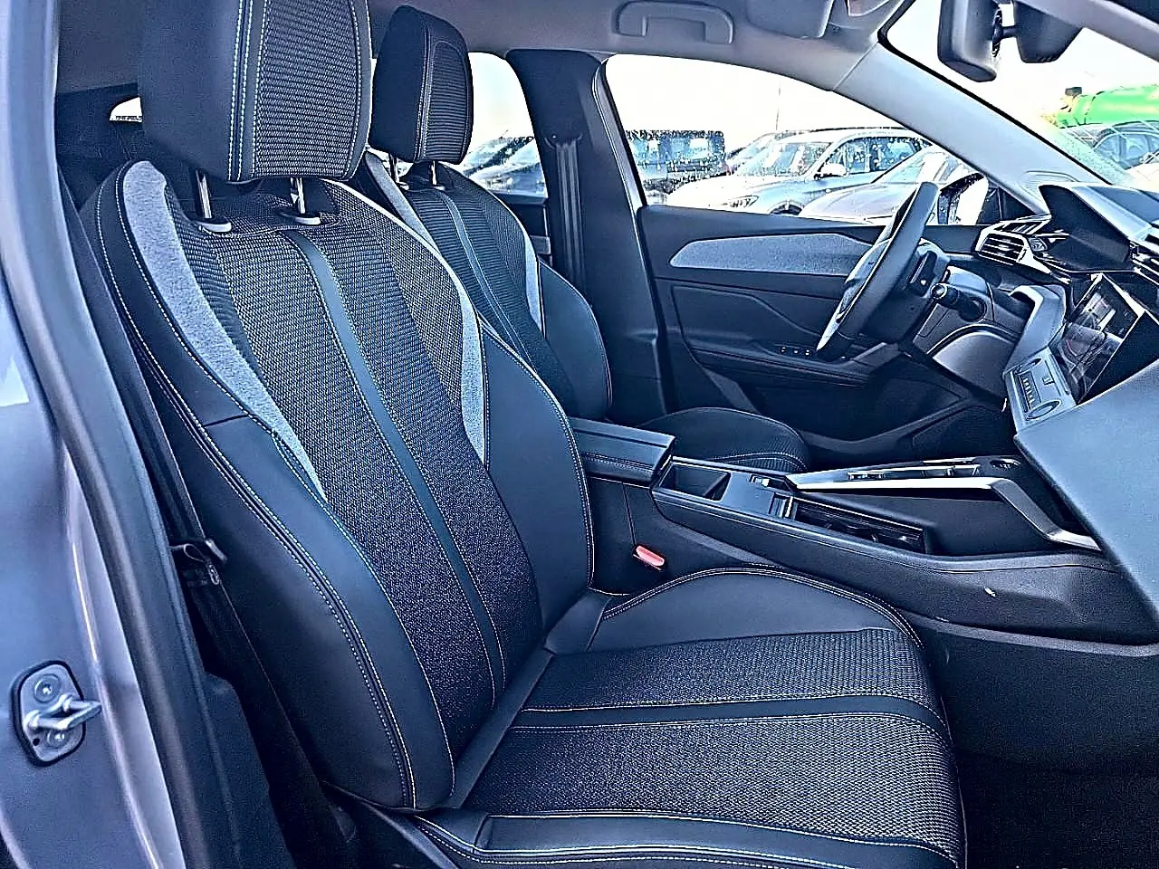 Vue intérieure côté conducteur de la Peugeot 308 SW 2025 gris artense, avec sièges tissu et cuir et accoudoir central.
