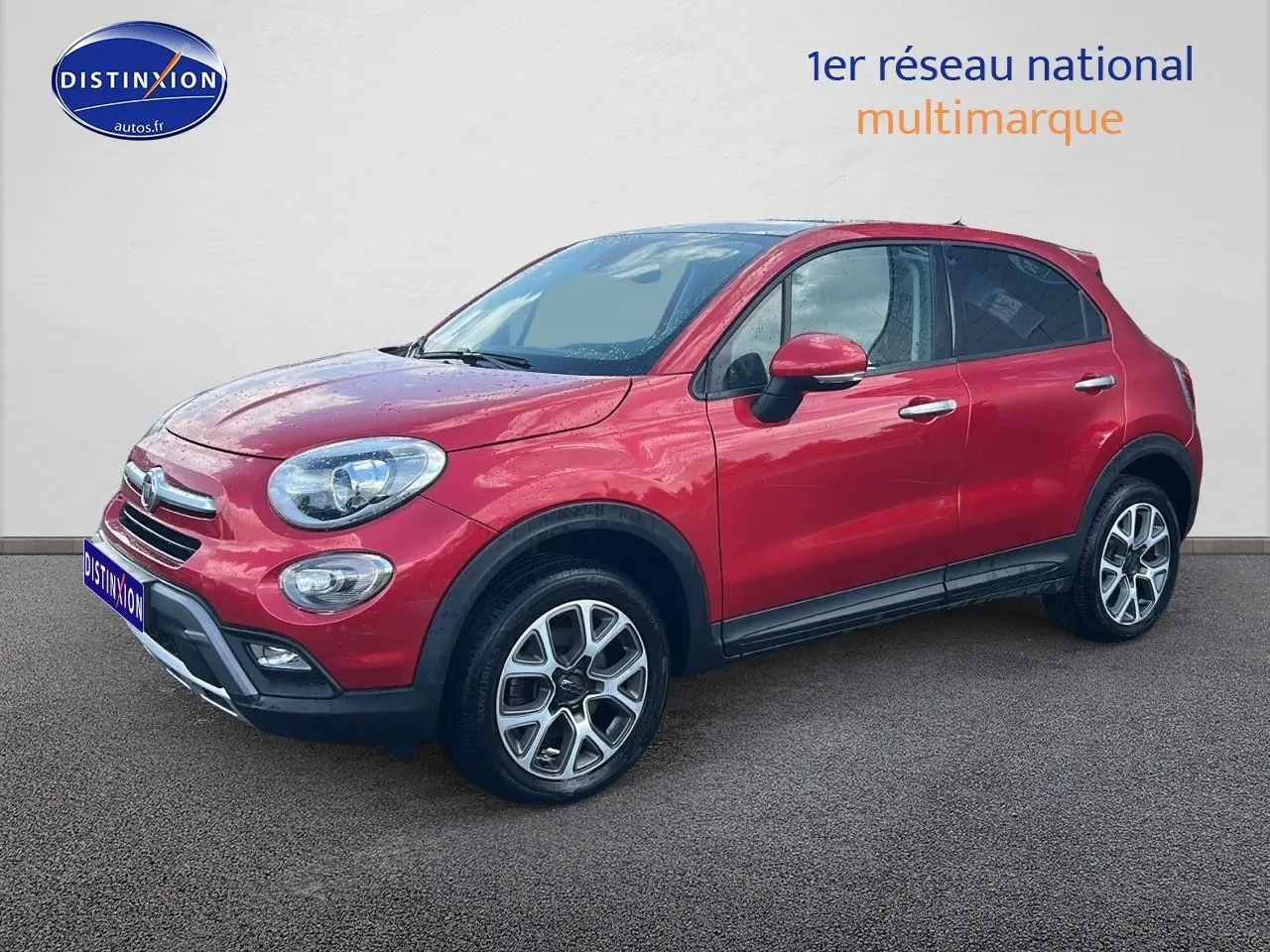 Vue 3/4 avant droite d'un FIAT 500X rouge avec jantes alu et barres de toit noires sur fond neutre.