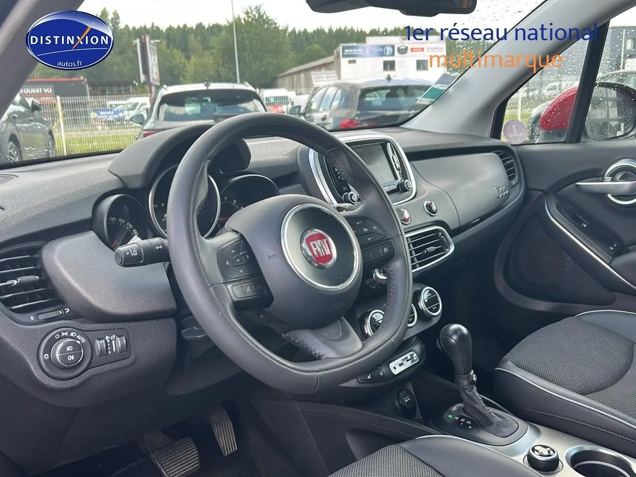 Intérieur de la Fiat 500X rouge, vue côté conducteur, volant cuir multifonction et tableau de bord moderne.