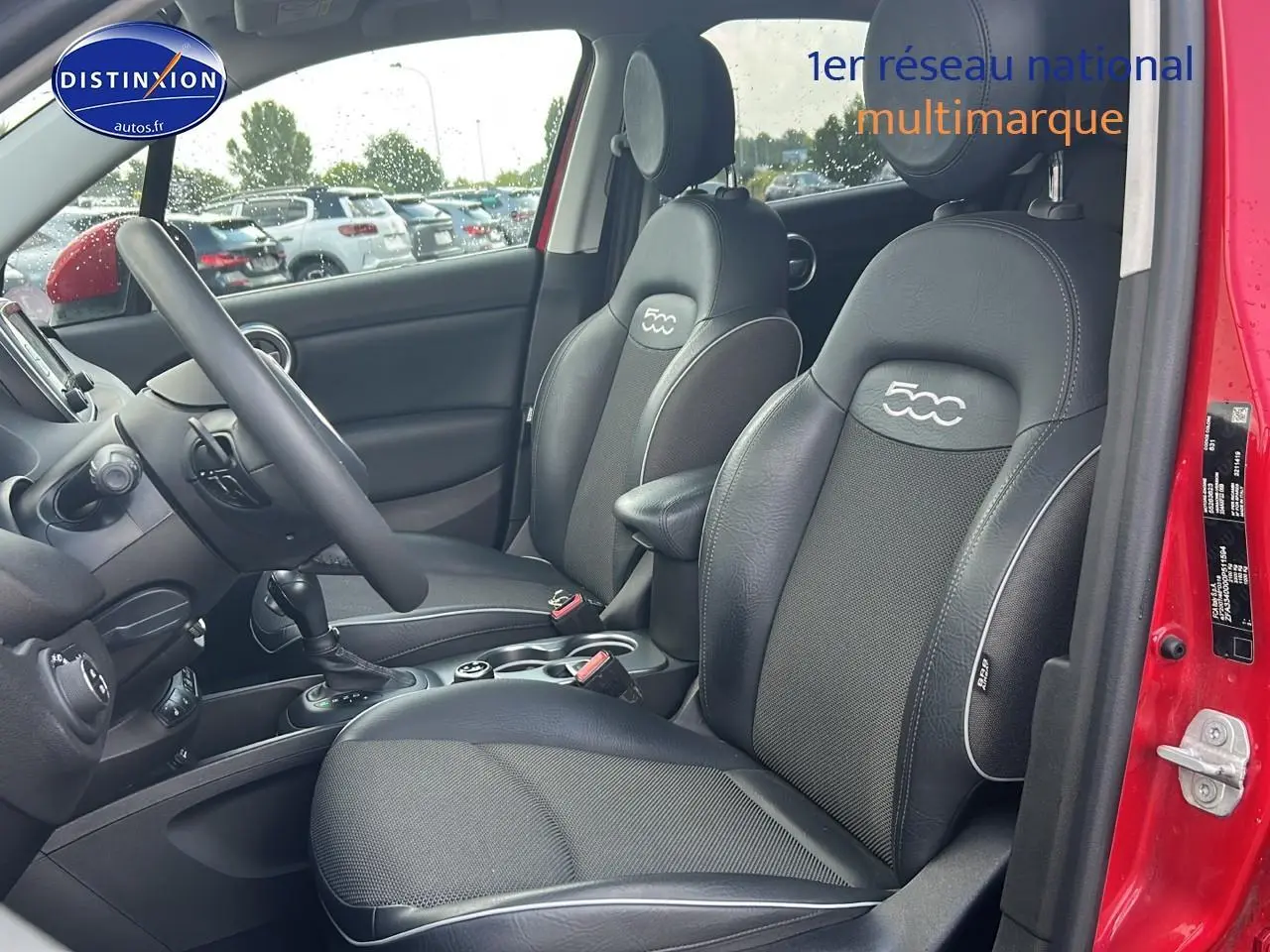 Vue intérieure côté conducteur d'une FIAT 500X rouge, sièges noirs avec logo 500 brodé sur les appuie-têtes.