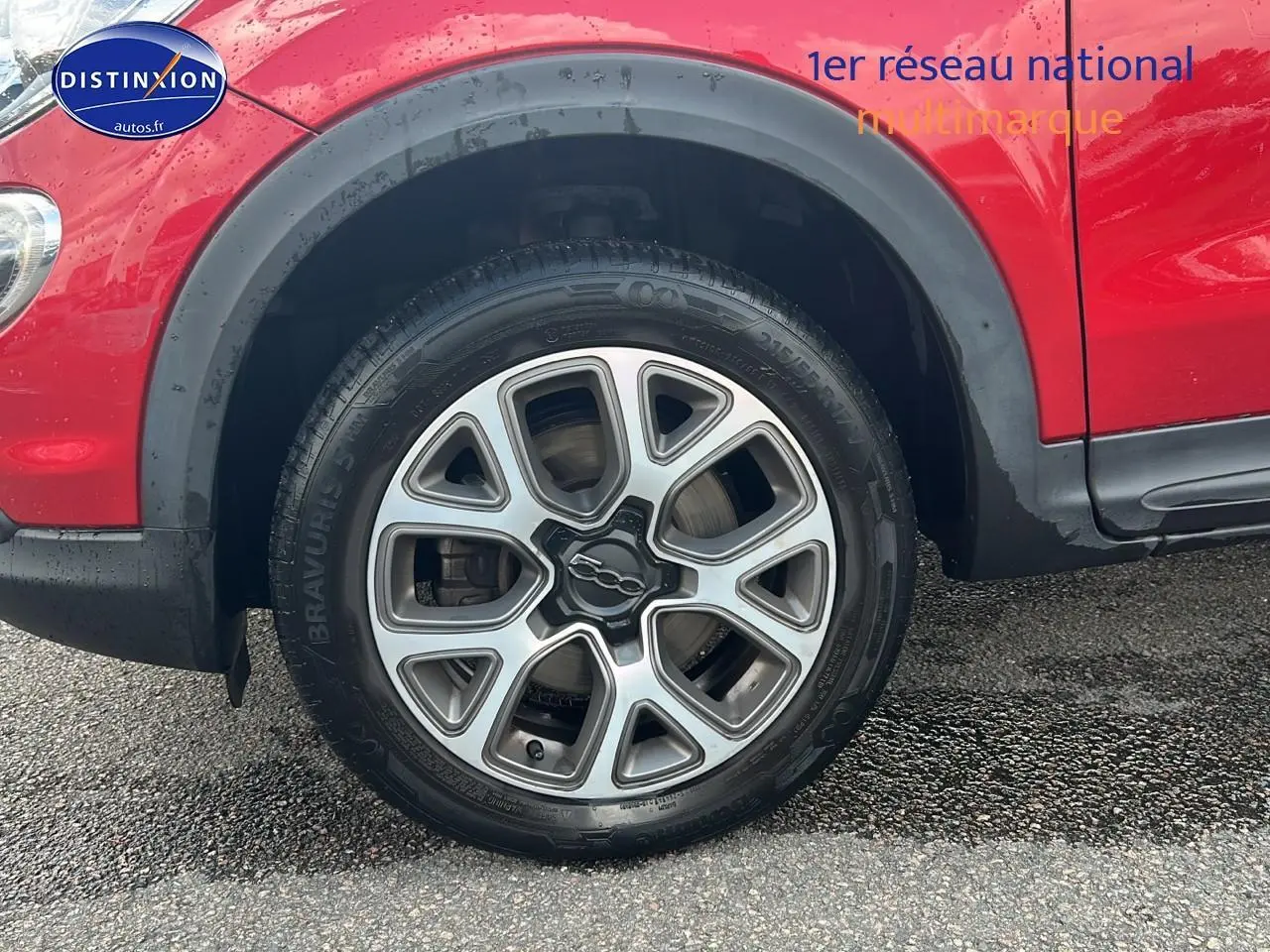 Gros plan sur la roue avant gauche rouge d'une Fiat 500X 2016 avec jante alu et entourage noir.