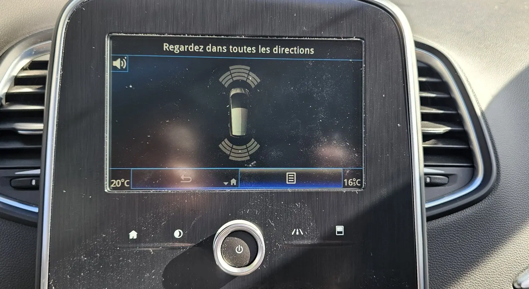 Écran central du tableau de bord d'une Renault Scénic 2020 affichant l'aide au stationnement, entouré d'aérateurs noirs.