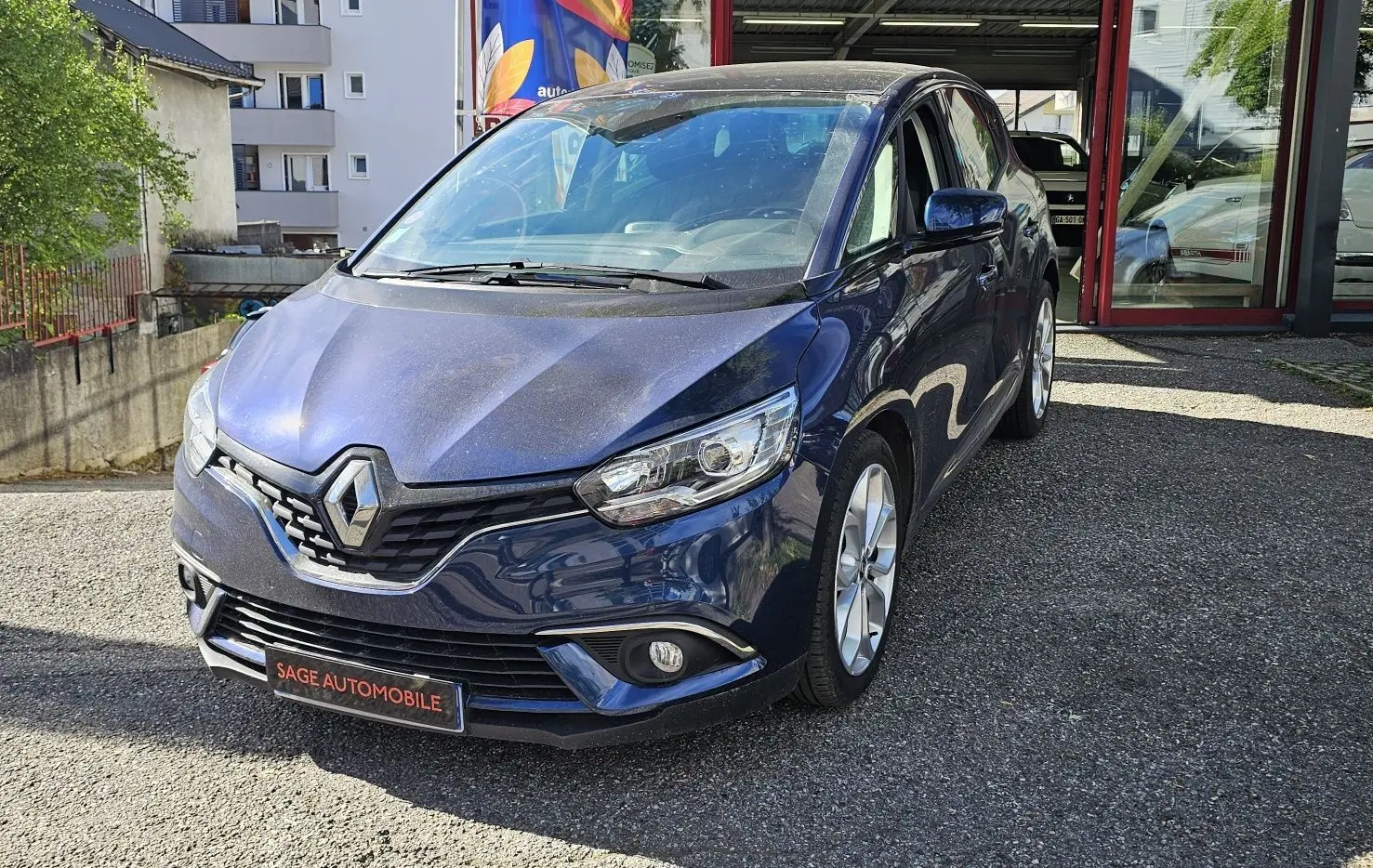 Renault Scénic bleu cosmos métal vu de 3/4 avant droit, avec calandre et phares modernes visibles.