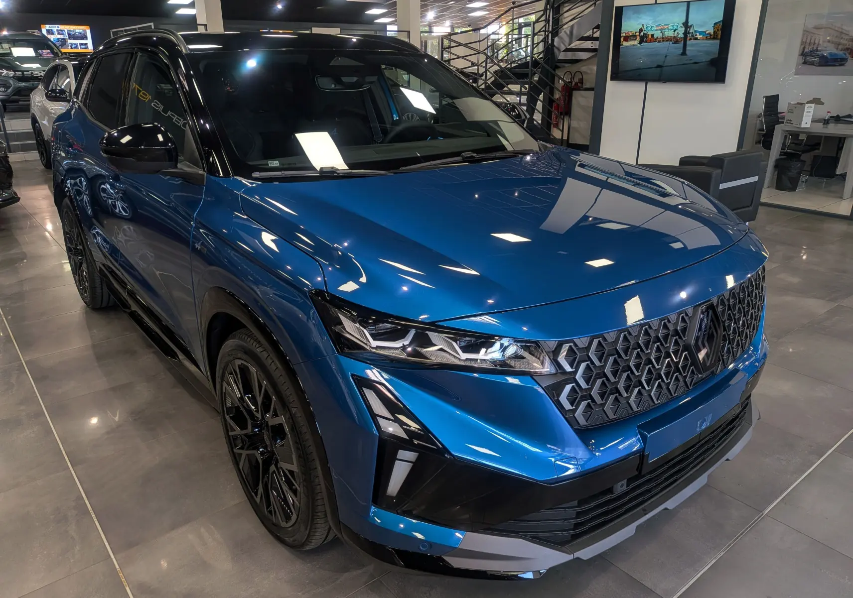 Vue 3/4 avant droit du Renault Austral 2025 bleu outremer avec toit noir et calandre hexagonale distinctive.