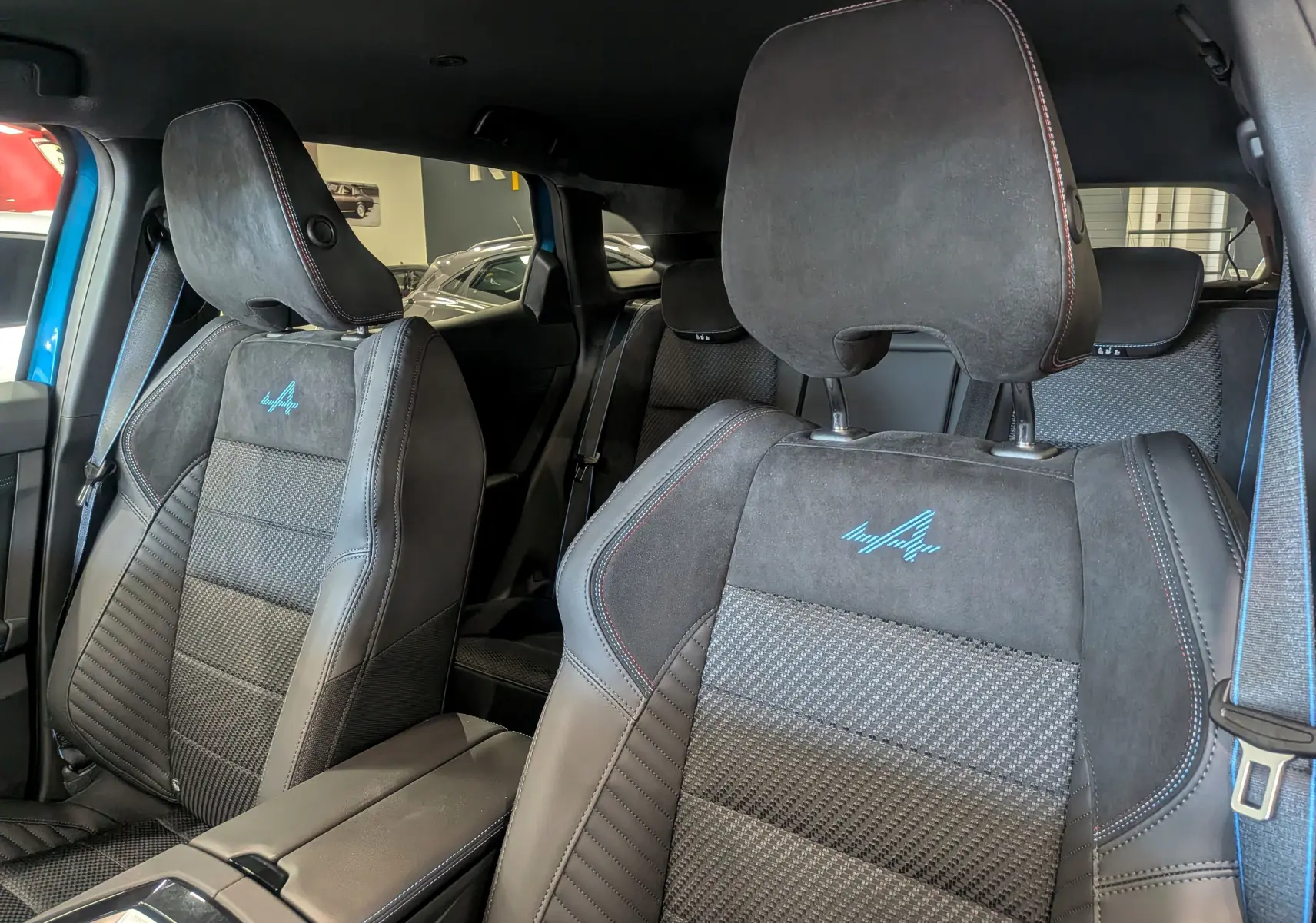 Gros plan sur les sièges avant en cuir noir avec logo Alpine bleu, intérieur du Renault Austral hybride 2025.