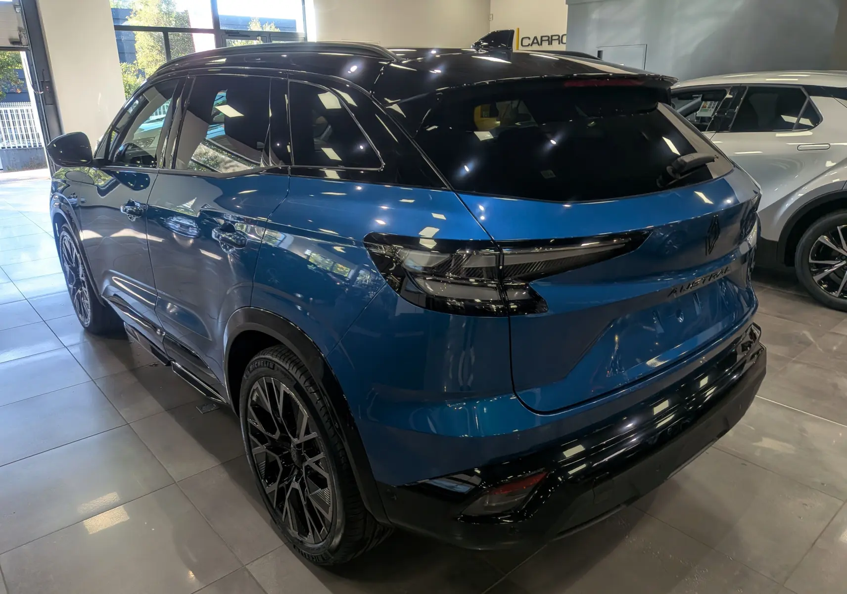 Vue 3/4 arrière droite du Renault Austral 2025 bleu outremer avec toit noir et jantes noires en showroom.