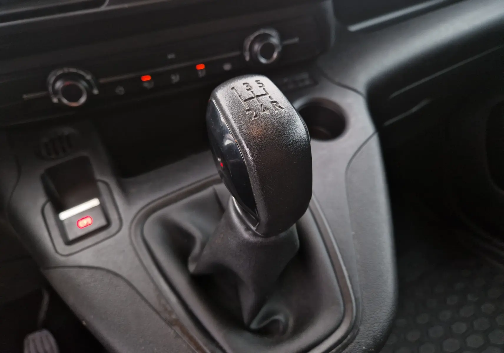 Gros plan sur le levier de vitesse manuel noir du Peugeot Partner blanc, avec tableau de bord et commandes en arrière-plan.