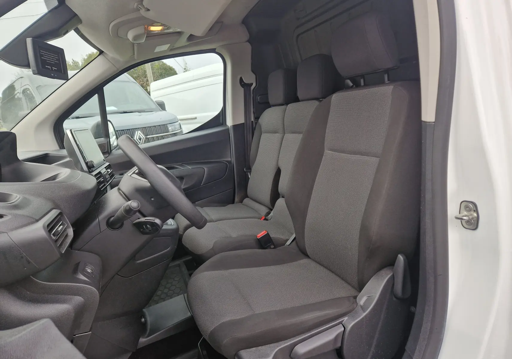 Vue intérieure côté conducteur du Peugeot Partner blanc 2020, montrant les sièges avant gris et le tableau de bord.