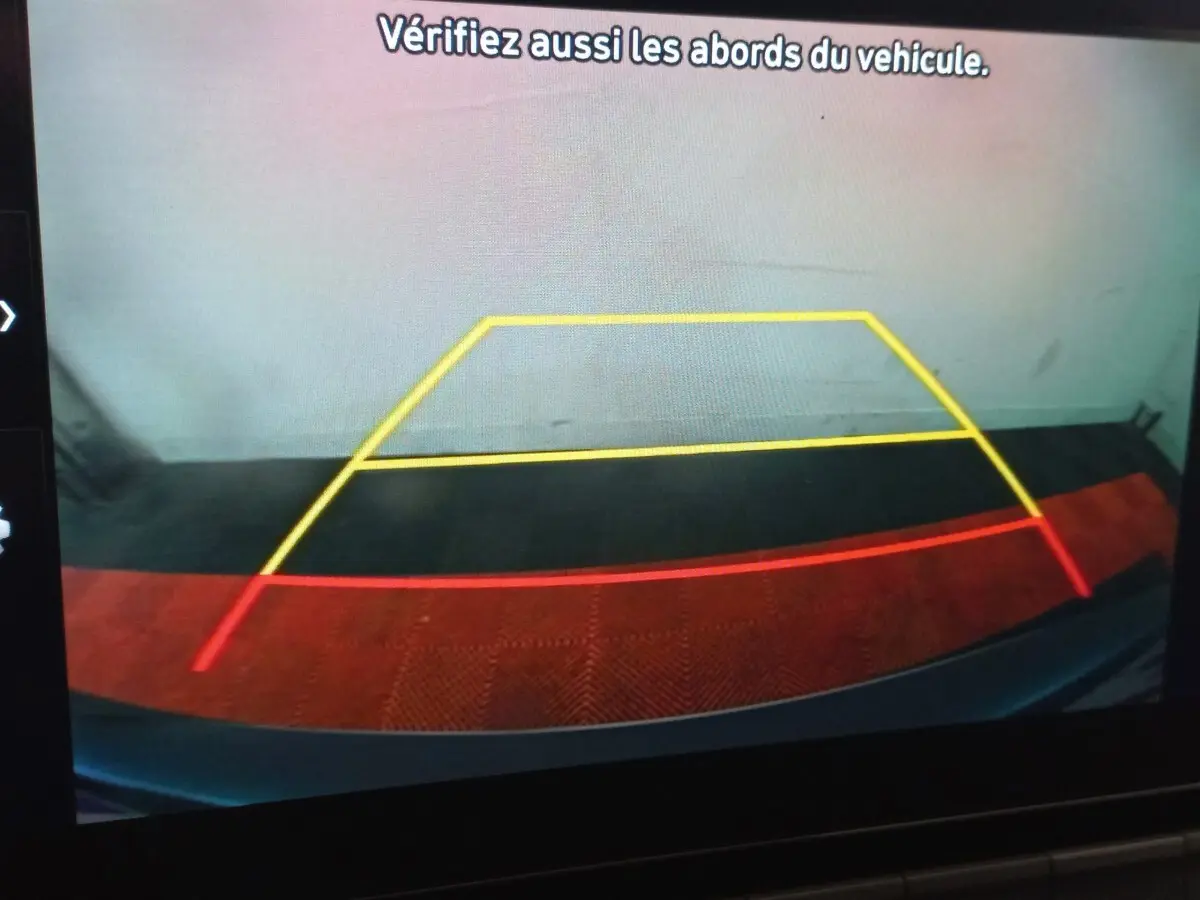 Vue caméra de recul du Hyundai Kona gris foncé, affichant les lignes de guidage jaune et rouge sur sol noir et rouge.