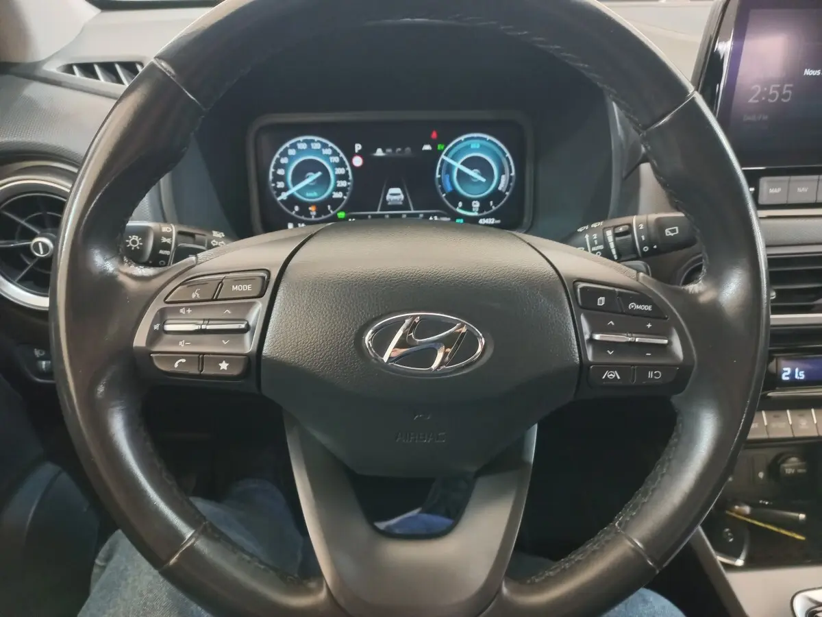 Vue rapprochée du volant cuir noir du Hyundai Kona 1.6 Hybrid 2022 avec commandes multifonctions et tableau de bord numérique.