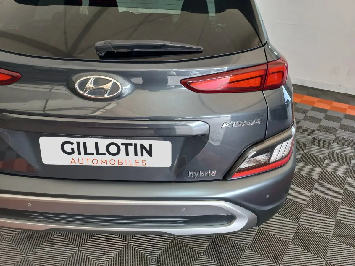 Vue arrière rapprochée du Hyundai Kona gris foncé avec logo, feux LED et badge hybrid visible sur un sol damier.