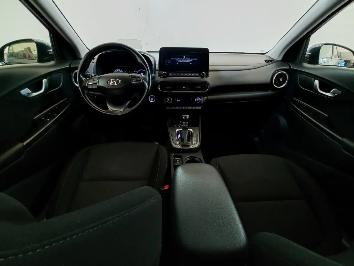 Vue intérieure avant du Hyundai Kona 1.6 Hybrid gris foncé, avec tableau de bord central tactile et volant multifonctions cuir.