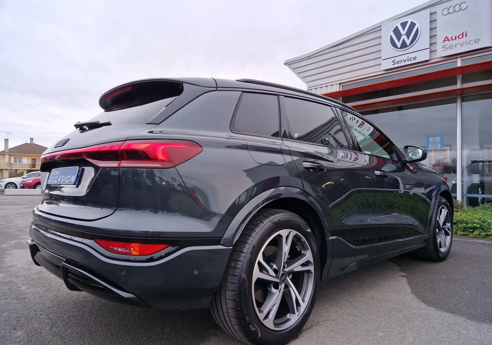 Audi Q6 e-tron Performance S-Line gris Manhattan, vue 3/4 arrière droit, feux arrière LED et jantes sport visibles.