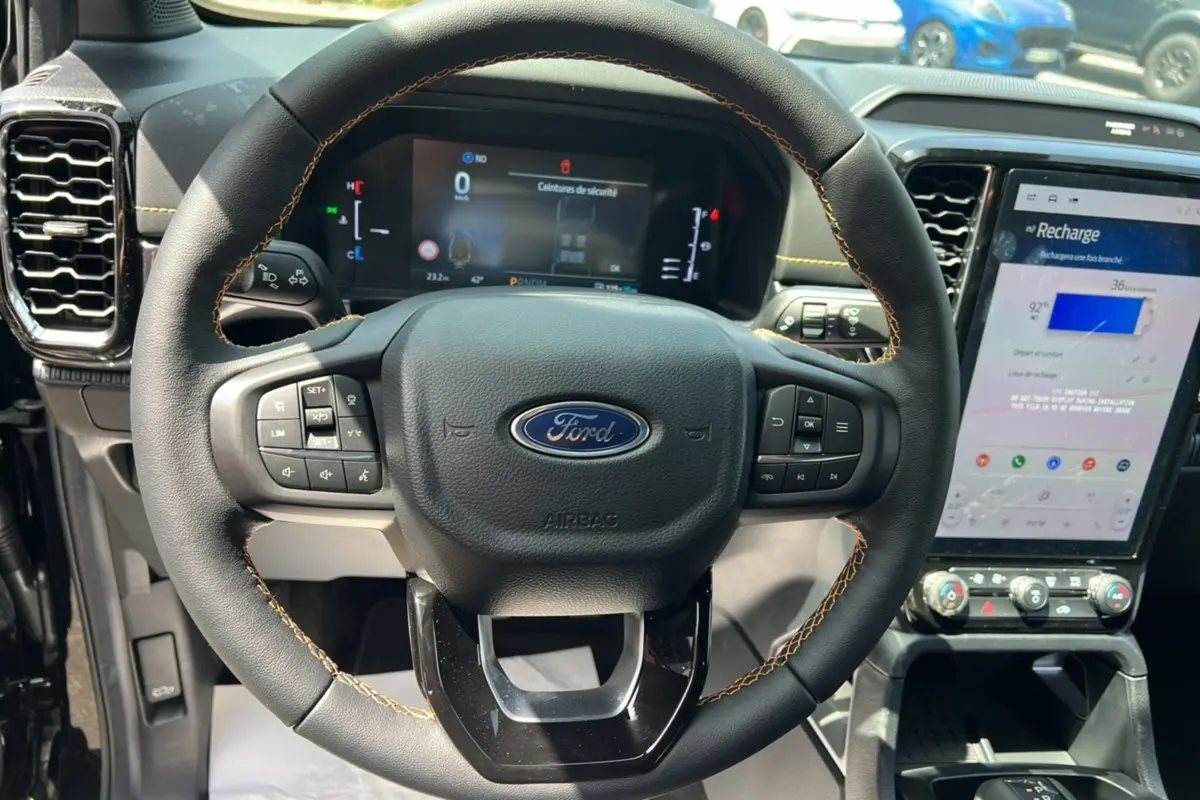 Vue rapprochée du volant cuir noir avec surpiqûres jaunes du Ford Ranger PHEV 2025, tableau de bord et écran tactile visibles.