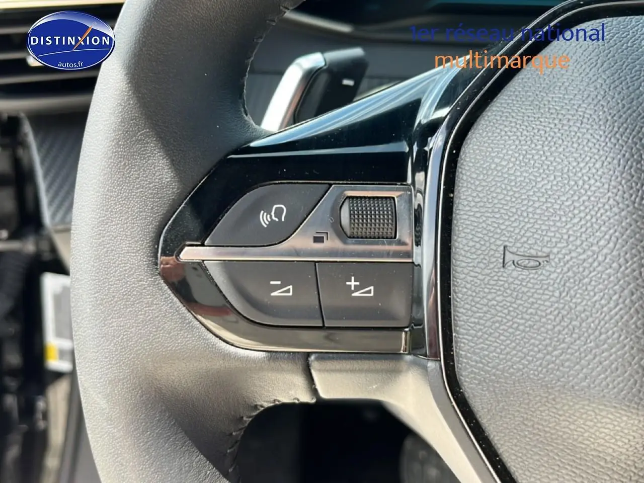 Gros plan sur les commandes gauche du volant noir du Peugeot 2008 1.2 hybrid 145 style e-dcs6, avec boutons de volume et appel mains-libres.