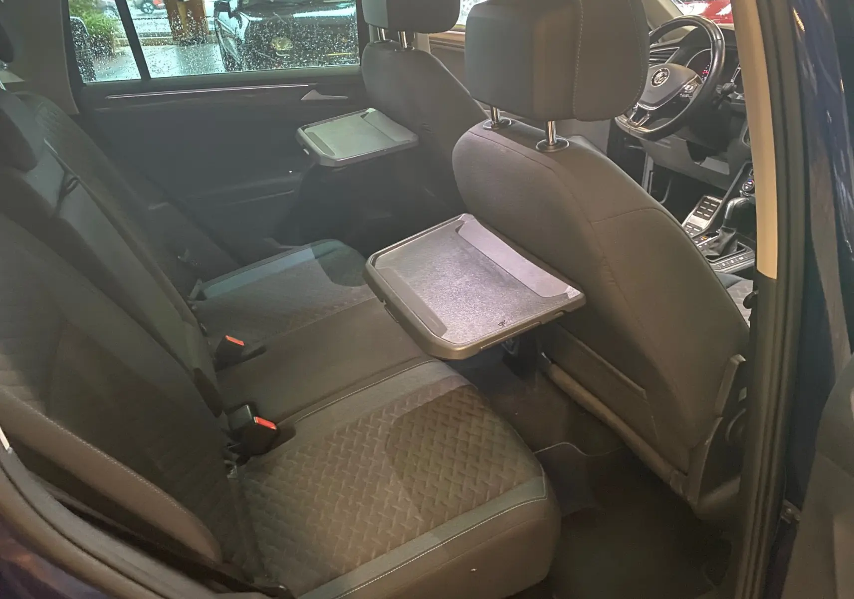 Vue intérieure arrière du Volkswagen Tiguan bleu vert 2020, sièges noirs avec tablettes pliantes intégrées aux dossiers avant.