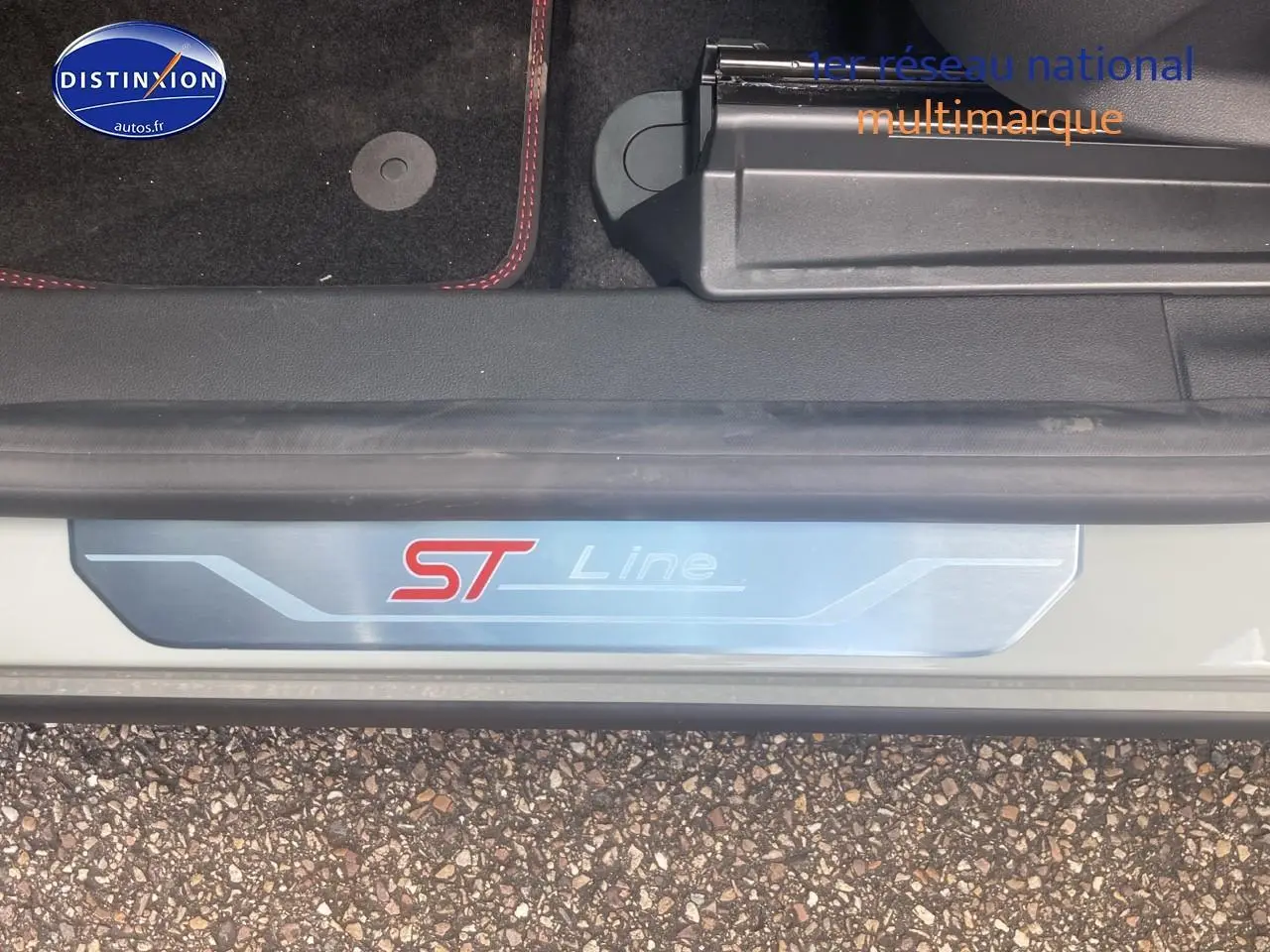 Gros plan sur la plaque de seuil ST Line du Ford Puma gris cactus, avec tapis noir et surpiqûres rouges visibles.