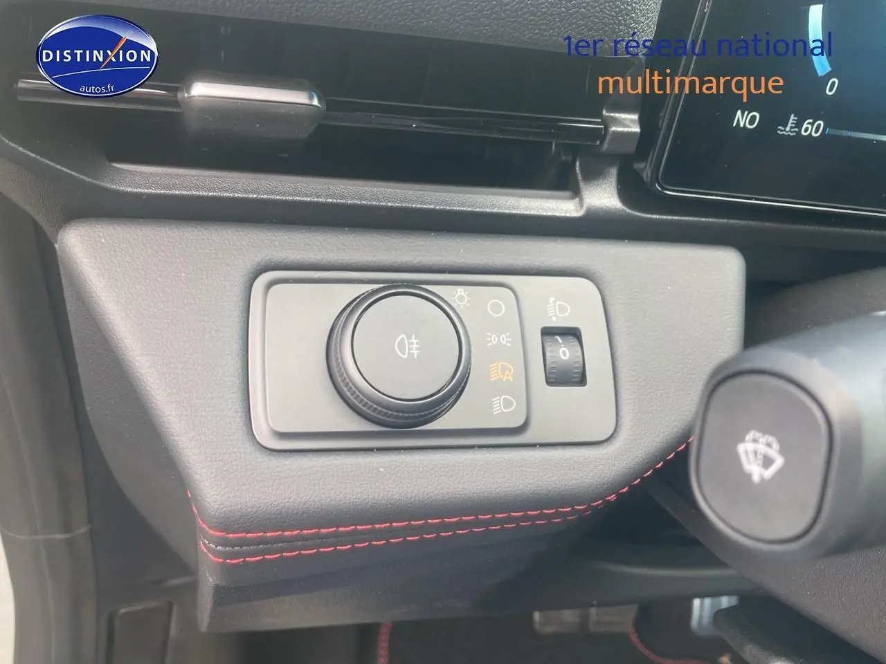 Gros plan sur le bouton de réglage des phares avec surpiqûres rouges sur le tableau de bord du Ford Puma gris cactus 2025.