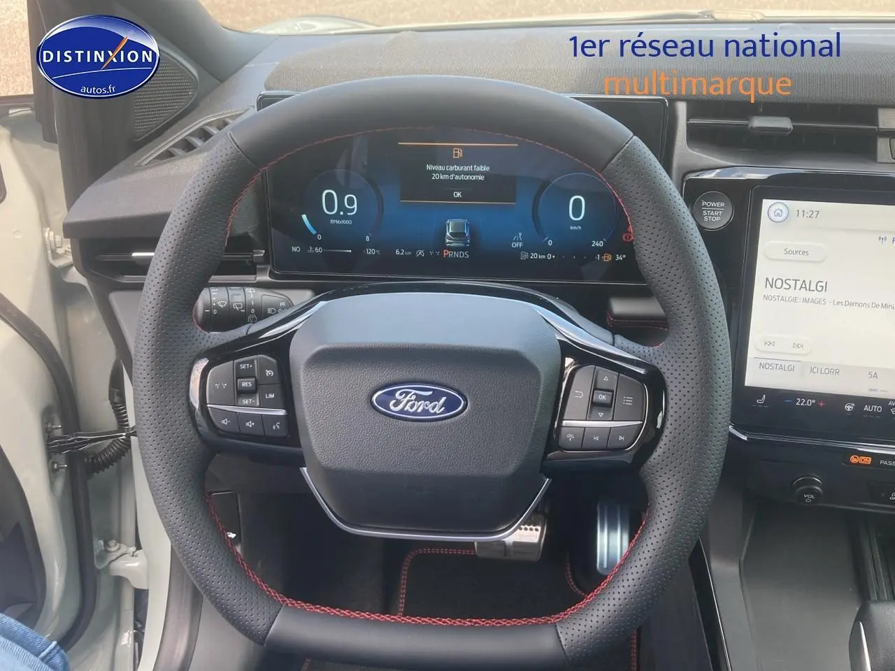 Vue rapprochée du volant perforé avec surpiqûres rouges et tableau de bord numérique du Ford Puma gris cactus 2025.