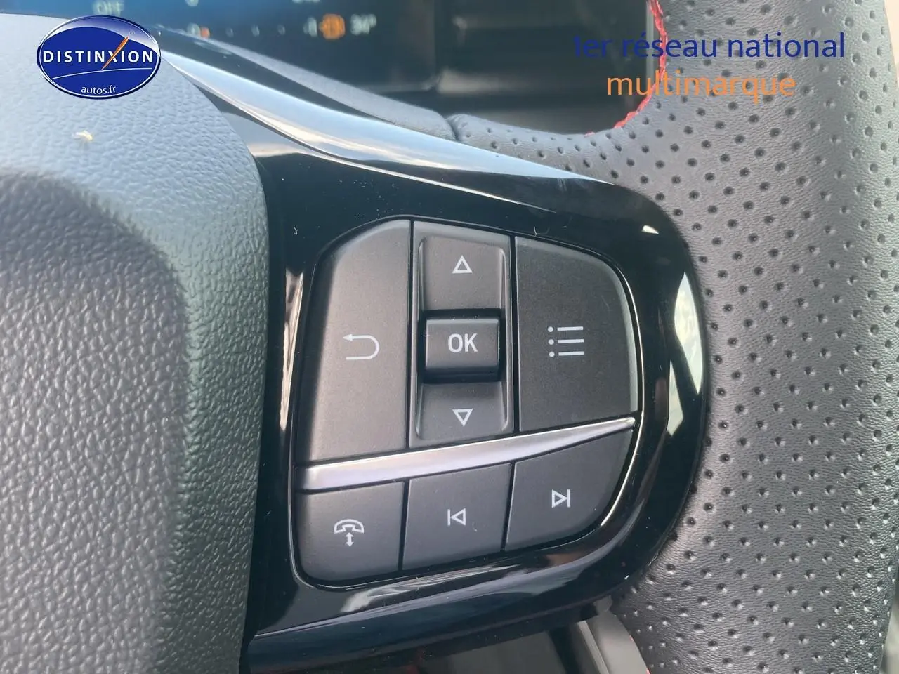 Gros plan sur les commandes multifonctions noires du volant perforé d'un Ford Puma gris cactus 2025.